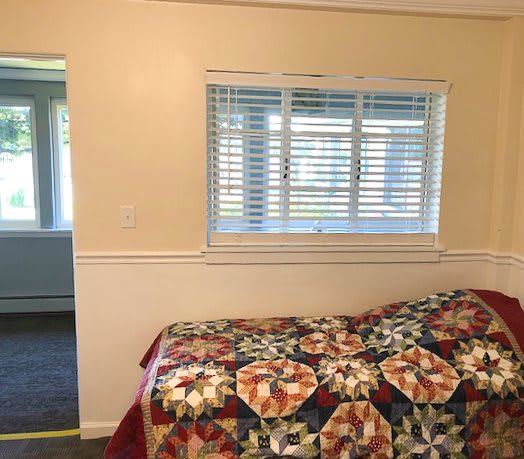 A cozy bedroom with a colorful quilt on the bed and sunlight streaming through the window blinds.