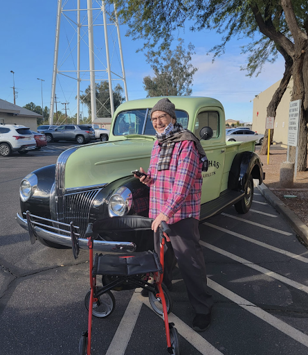 An elderly person stands next to a vintage green truck in a parking lot.