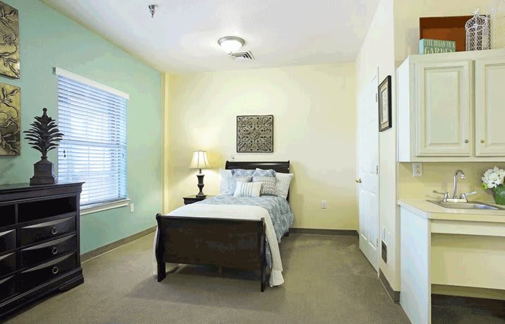 A cozy bedroom with a bed, lamp, and window, featuring soft lighting and simple decor.