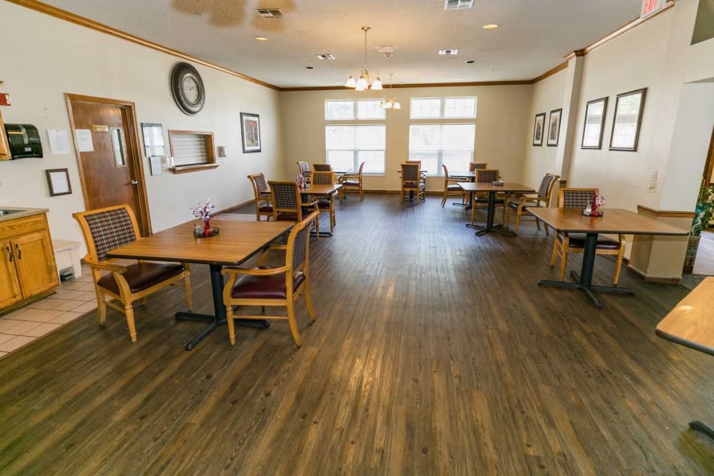 A spacious dining room featuring wooden floors, multiple tables and chairs, and large windows allowing natural light to fill the space.