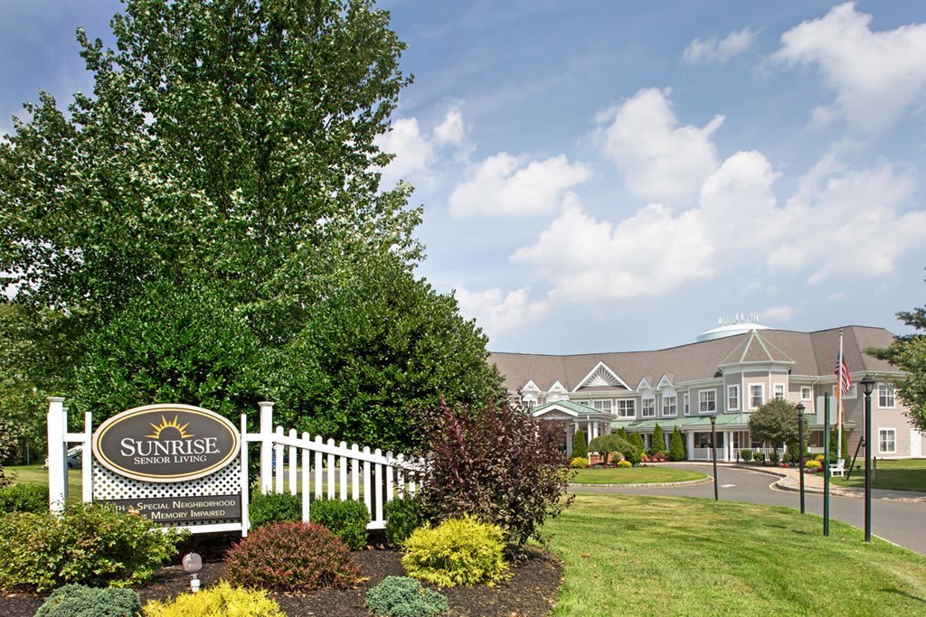 A scenic view of a structured building with manicured landscaping and an entrance sign under a partly cloudy sky.