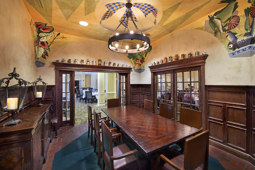 A traditional dining room featuring a large wooden table surrounded by chairs, with elegant decor and a chandelier overhead.