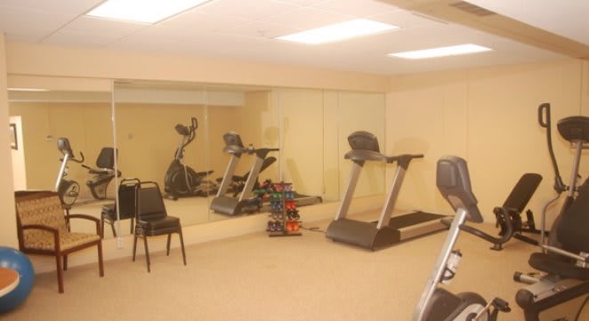 A small gym with exercise equipment including treadmills, an elliptical machine, and a set of dumbbells.
