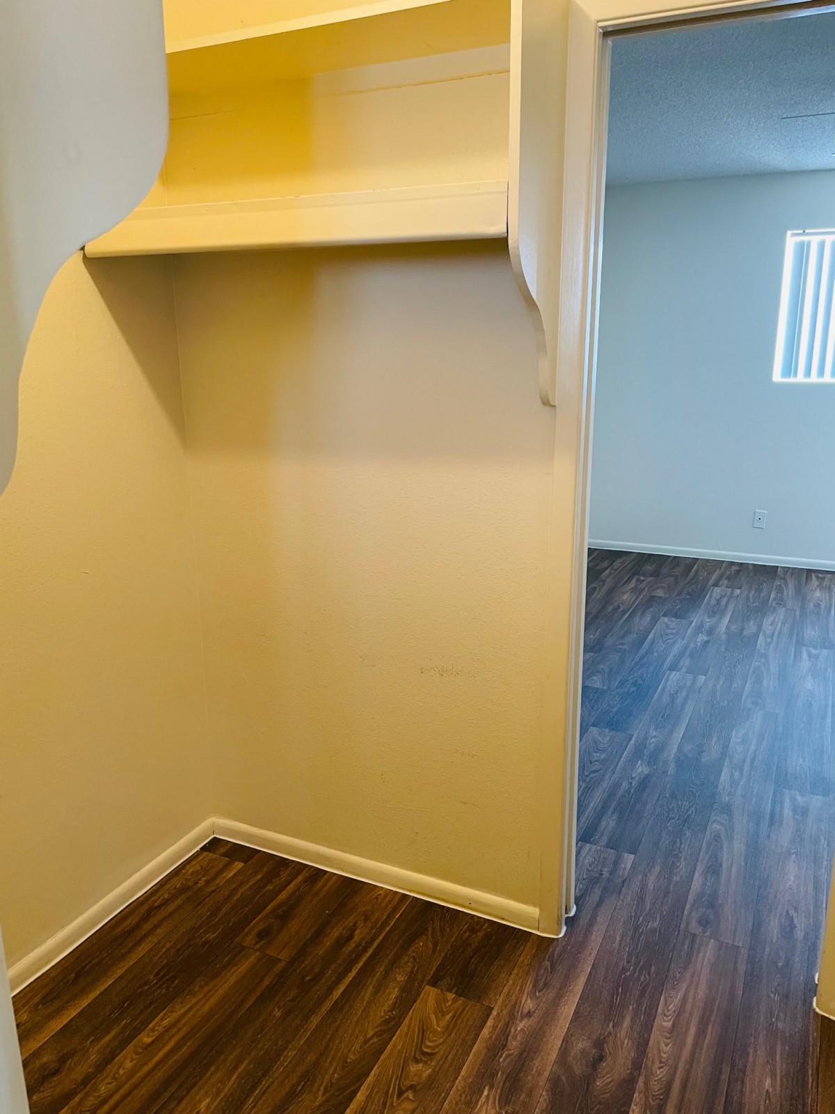 An empty interior space with a closet featuring a built-in shelf and wooden flooring.