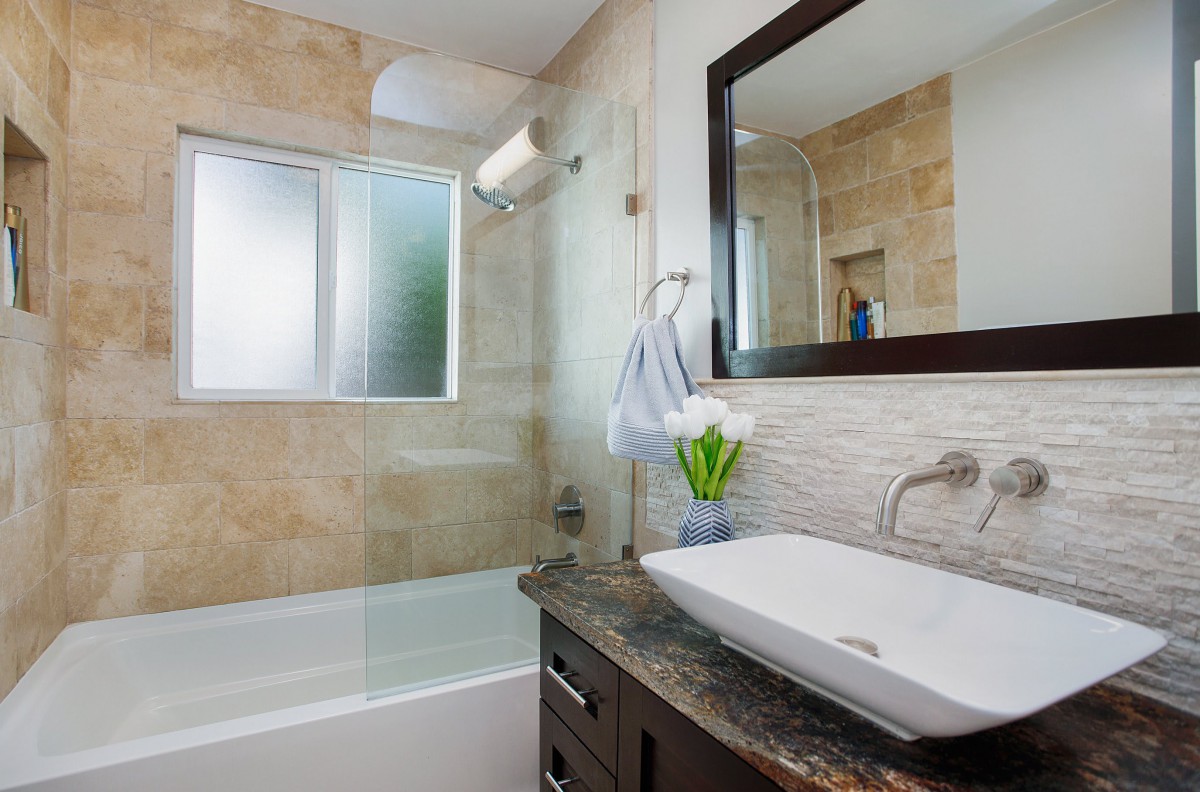 A modern bathroom featuring a stylish sink, large mirror, and a bathtub with a glass partition.