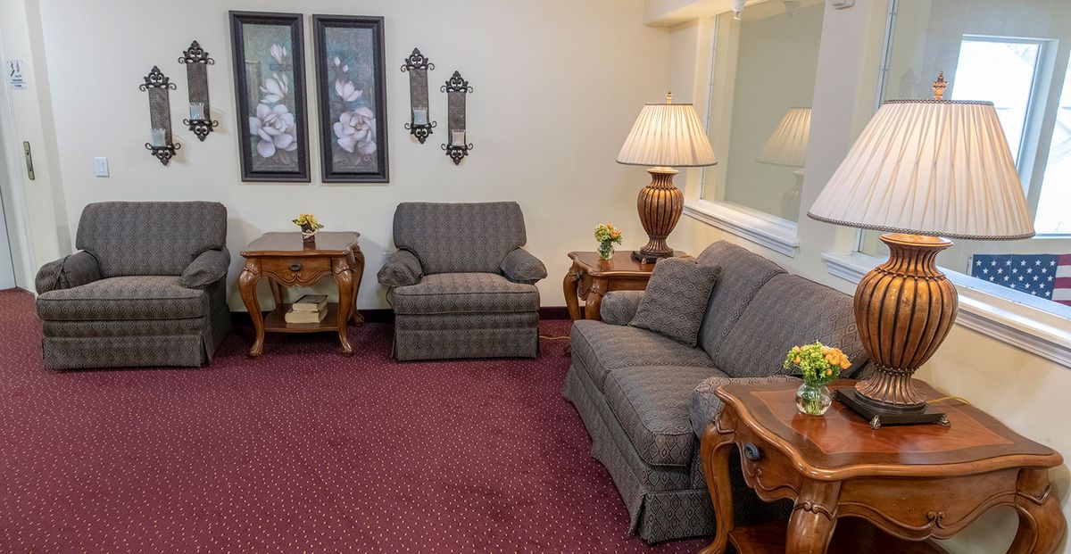 A cozy living room with a sofa, armchair, side tables, lamp, and decorative wall art.