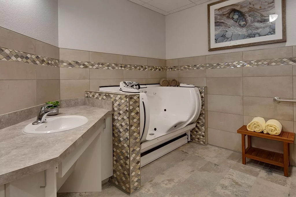 A modern bathroom featuring an accessible bathtub with a tiled surround, a sink, and decorative elements.