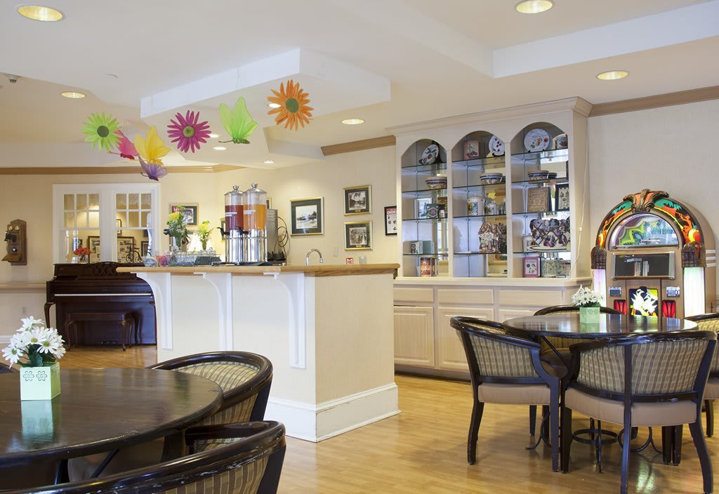 A cozy cafe interior with tables and chairs, colorful decorations, beverage dispensers, and wooden flooring.