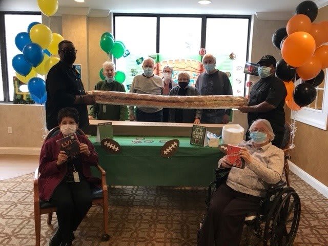 A group of people celebrating indoors with balloons and a large sandwich.