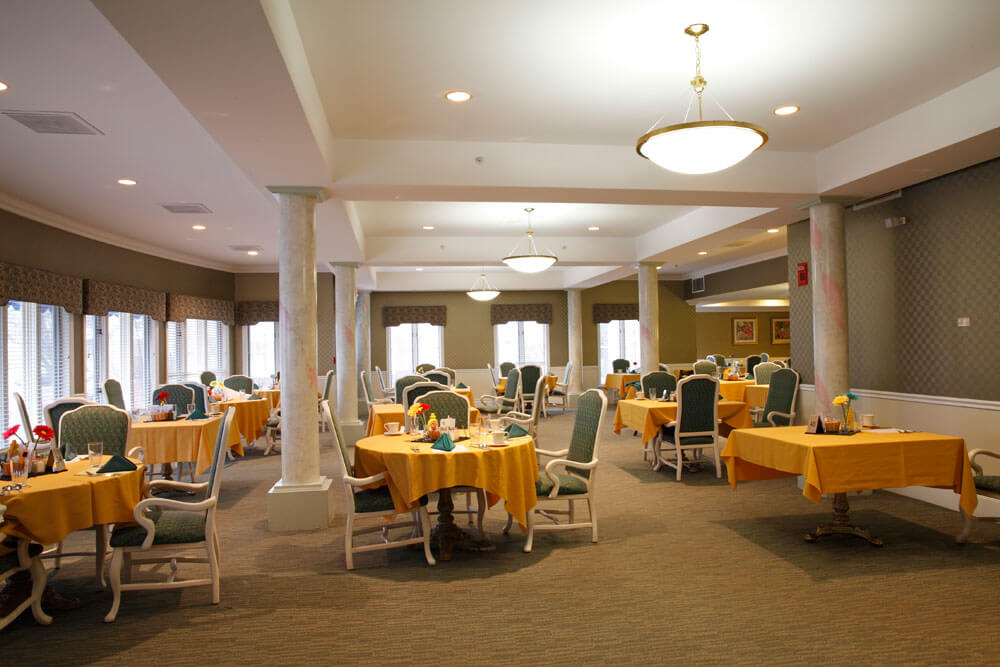 A spacious dining room with neatly arranged tables covered in yellow tablecloths.