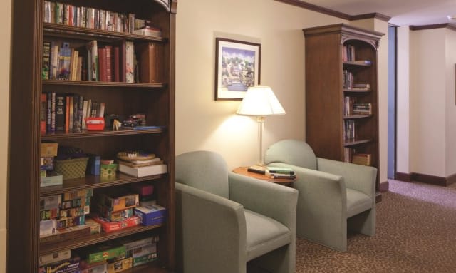 A cozy reading nook with bookshelves, chairs, and a lamp.