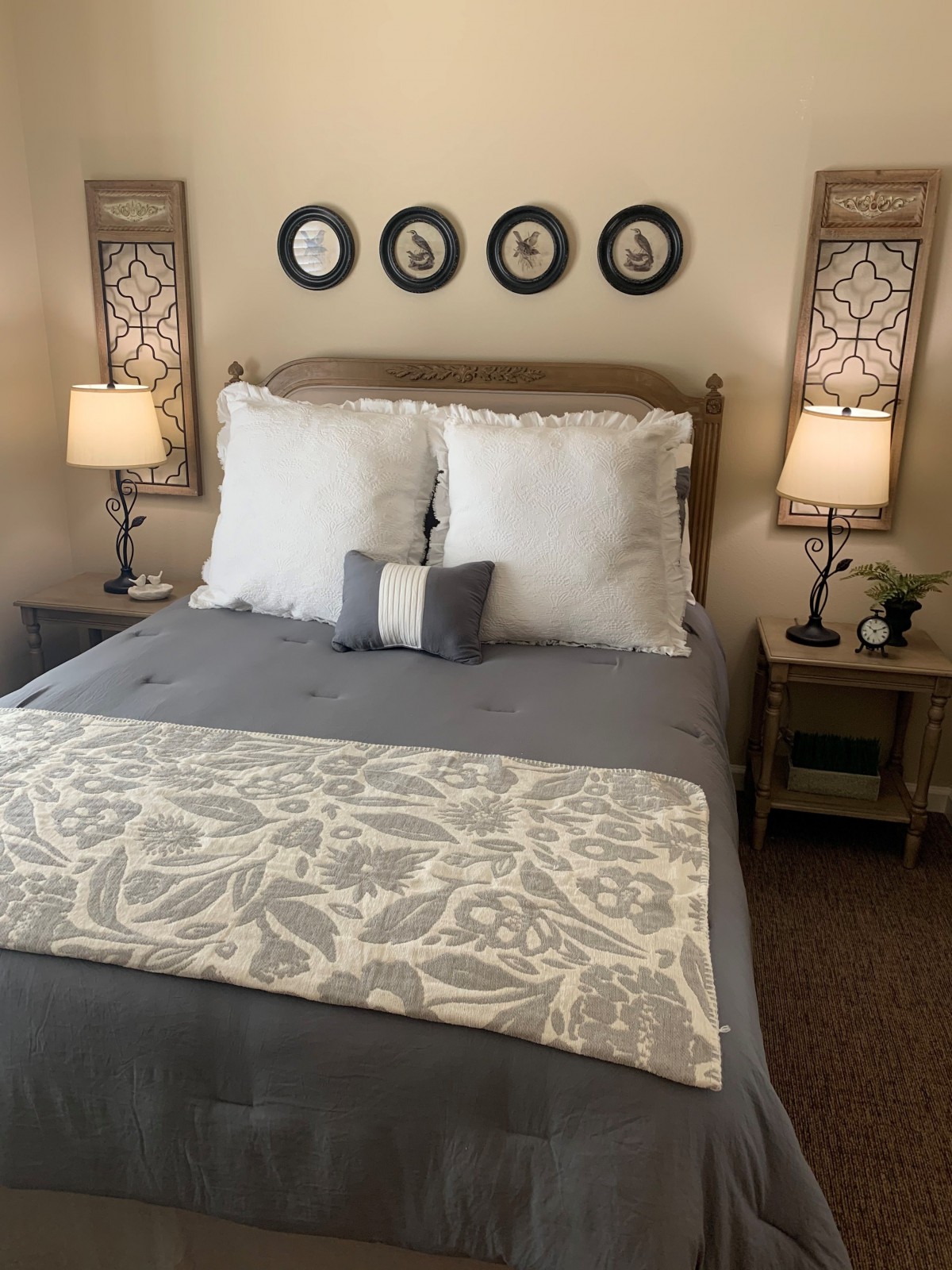 A well-decorated bedroom with a neatly made bed, flanked by nightstands and lamps, featuring wall art above the headboard.