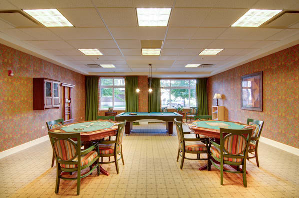 A spacious game room with multiple tables and chairs, featuring large windows and stylish lighting.