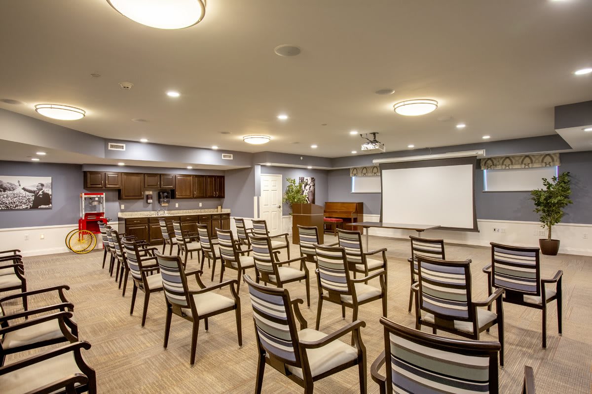 A well-lit conference room equipped with arranged chairs and a projector screen for presentations.