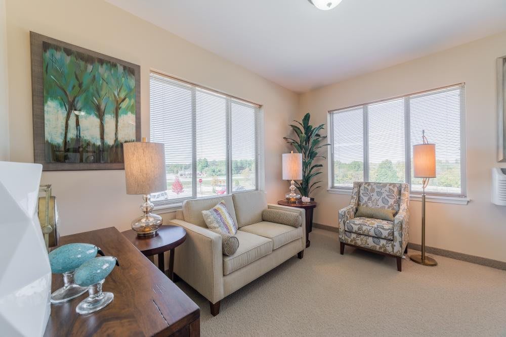 A cozy living room with a sofa, armchair, and soft lighting from lamps near large windows.