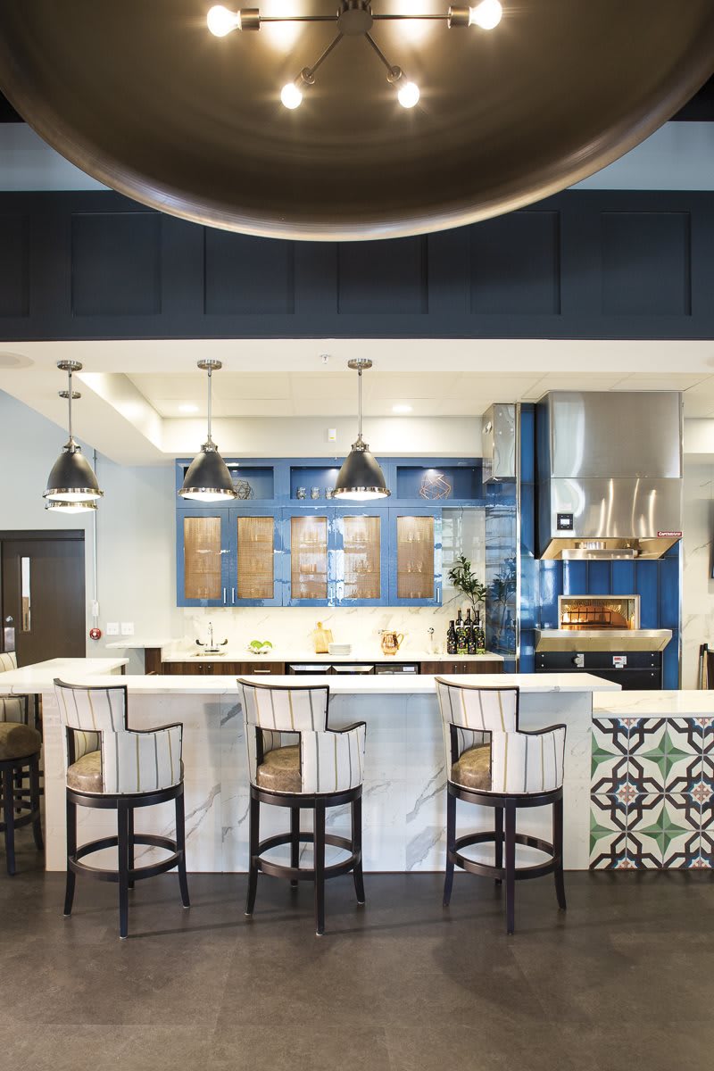 A modern kitchen with blue cabinets, pendant lights, and bar stools.