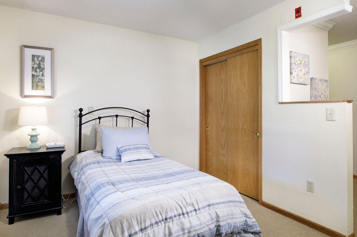 A simple bedroom with a single bed and striped bedding next to a wooden closet.