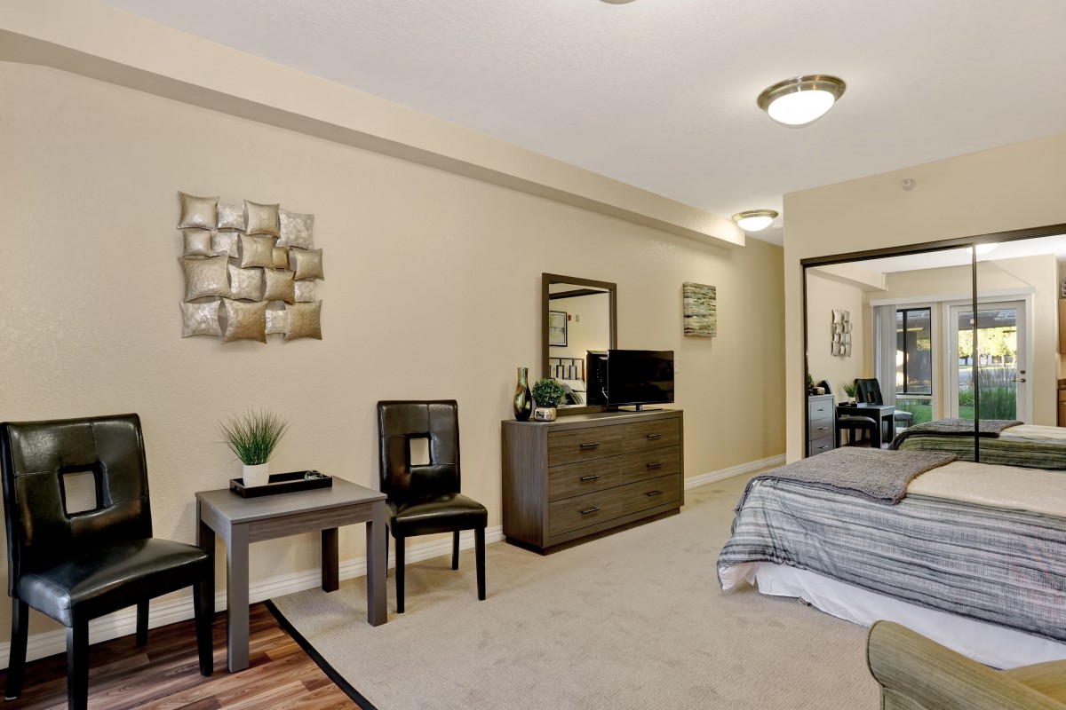 A modern bedroom with a neatly arranged interior, featuring a bed, dresser with mirror, TV, and decorative elements.