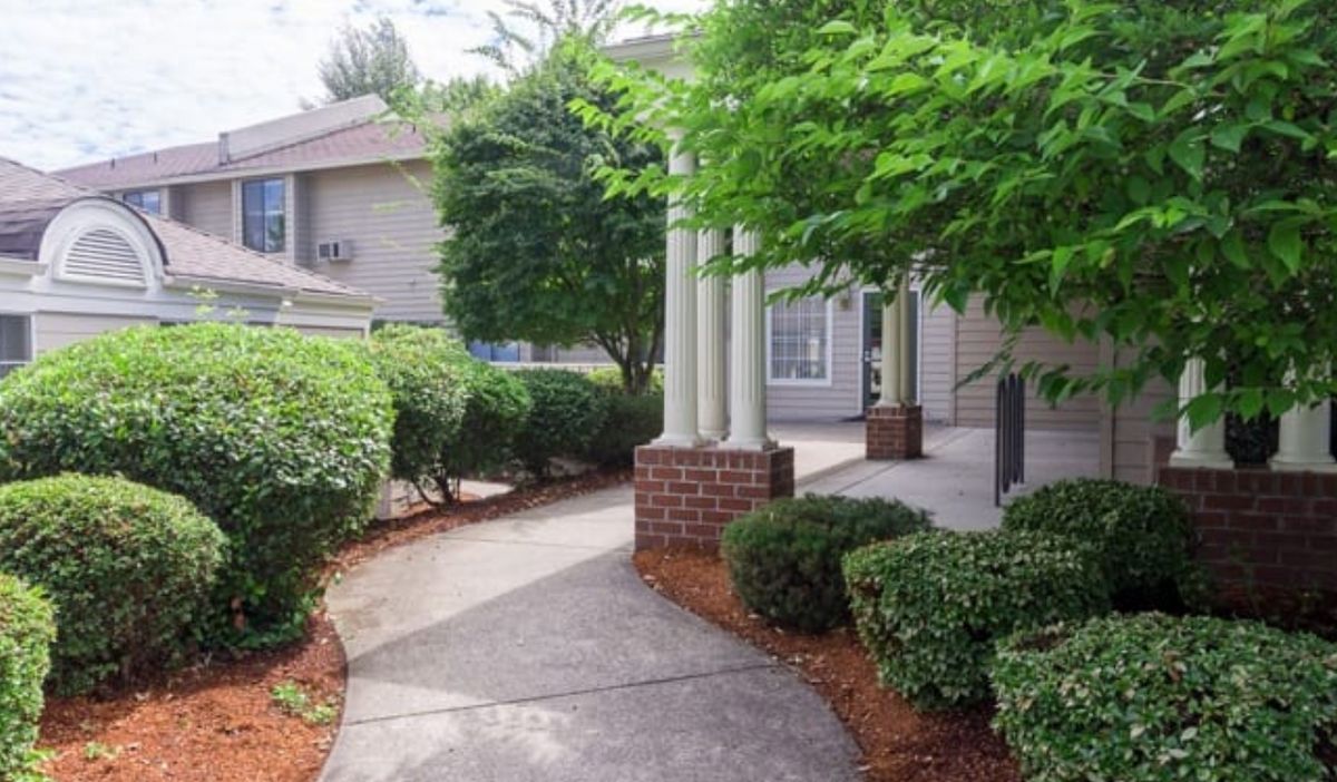 A walkway surrounded by lush greenery leads to the entrance of a residential building.