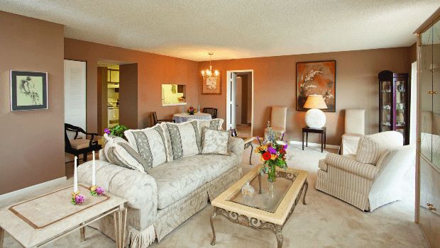 A cozy living room with a patterned sofa, wooden coffee table, and decorative elements like flowers and a painting.