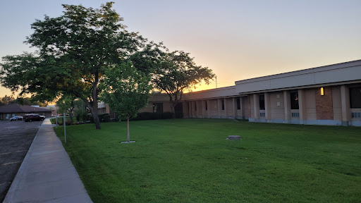A peaceful view of a building surrounded by lush green grass and a tree, illuminated by the warm colors of the sunset.