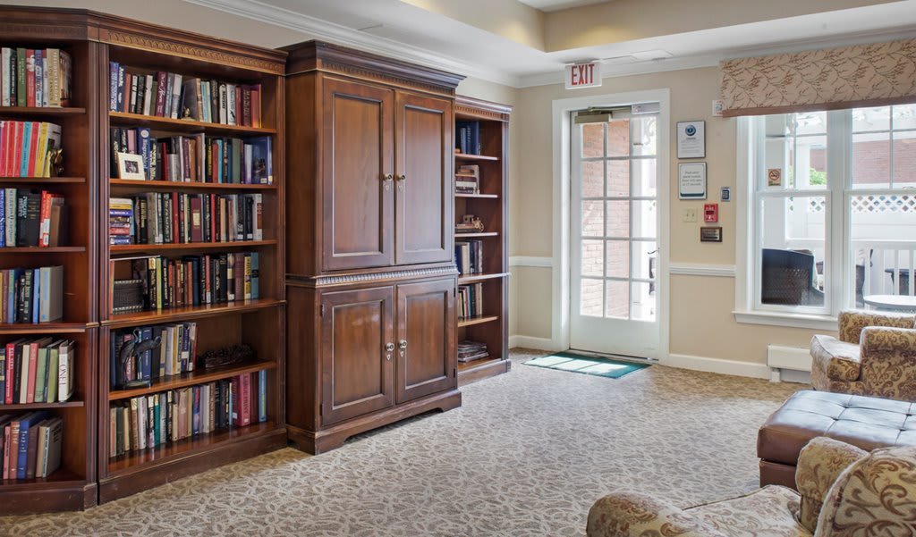 A cozy library interior with wooden bookshelves and a cabinet next to a glass door.