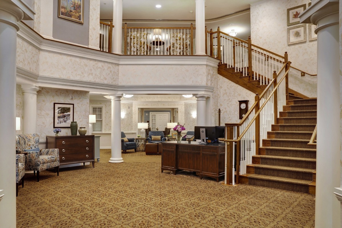 A spacious hotel lobby featuring a grand staircase, elegant furniture, and decorative columns.