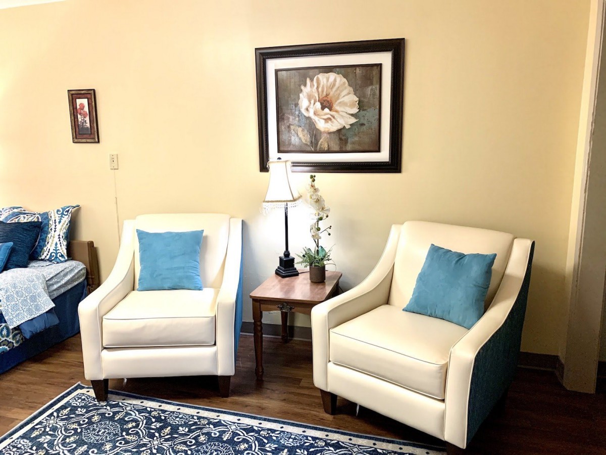 A cozy living room setup featuring two cream armchairs with blue cushions, accompanied by a lamp and wall art.