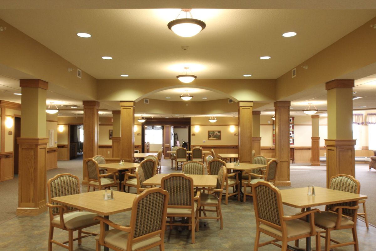 An empty dining area with multiple tables and chairs, featuring warm lighting.