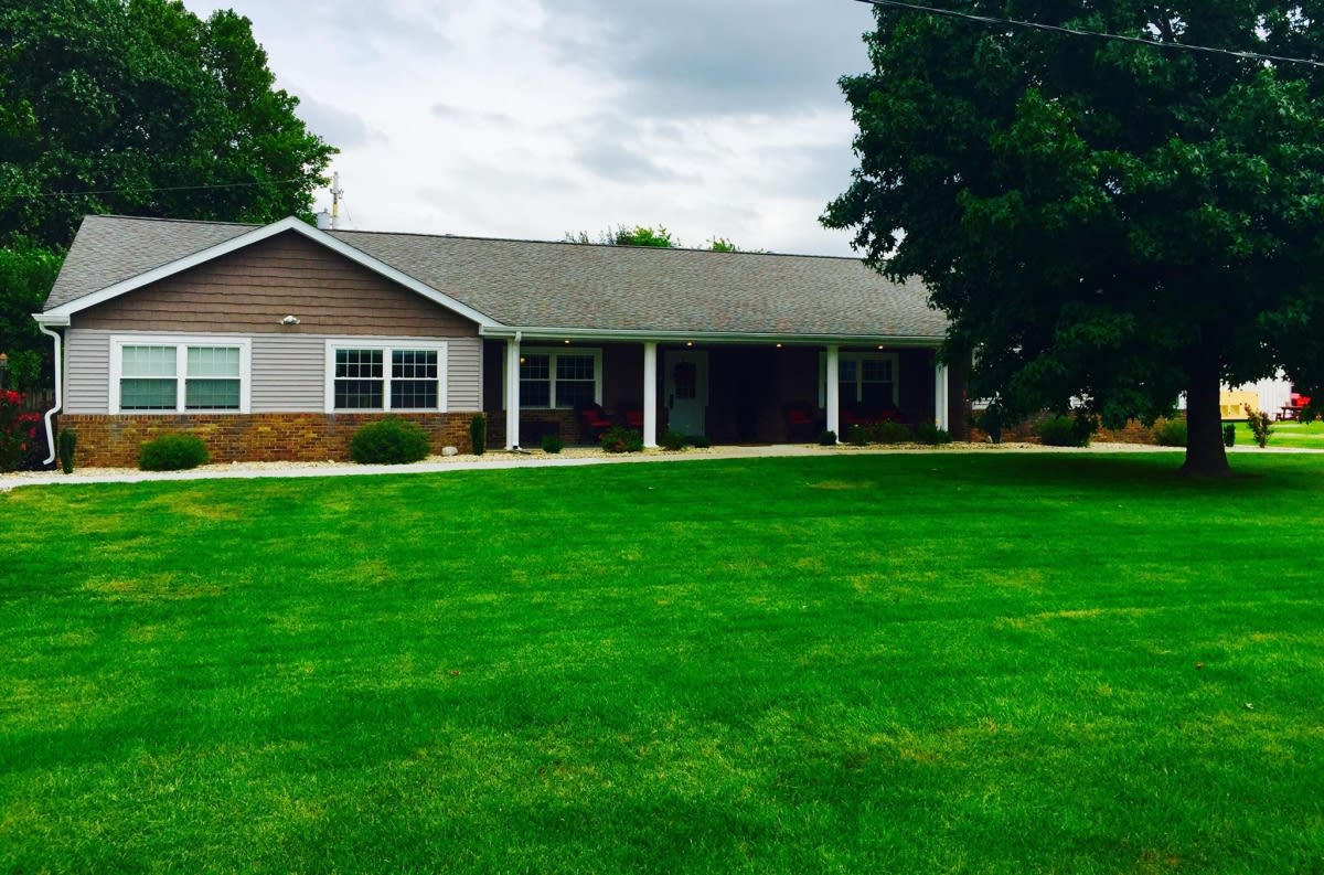 A suburban house with a large green lawn and trees under a cloudy sky.