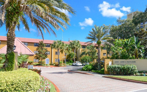 A welcoming hotel entrance lined with palm trees under a clear blue sky.