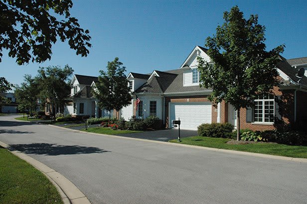 A quiet suburban street lined with houses and trees on a sunny day.