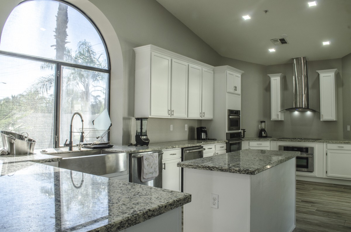 A modern kitchen with white cabinets, granite countertops, and a large window providing natural light.