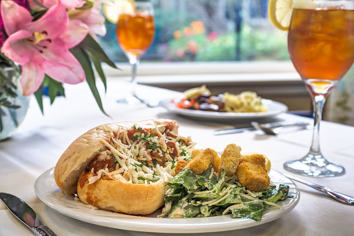 A delicious sandwich served with salad and fried sides on a neatly arranged dining table, accompanied by a refreshing drink.
