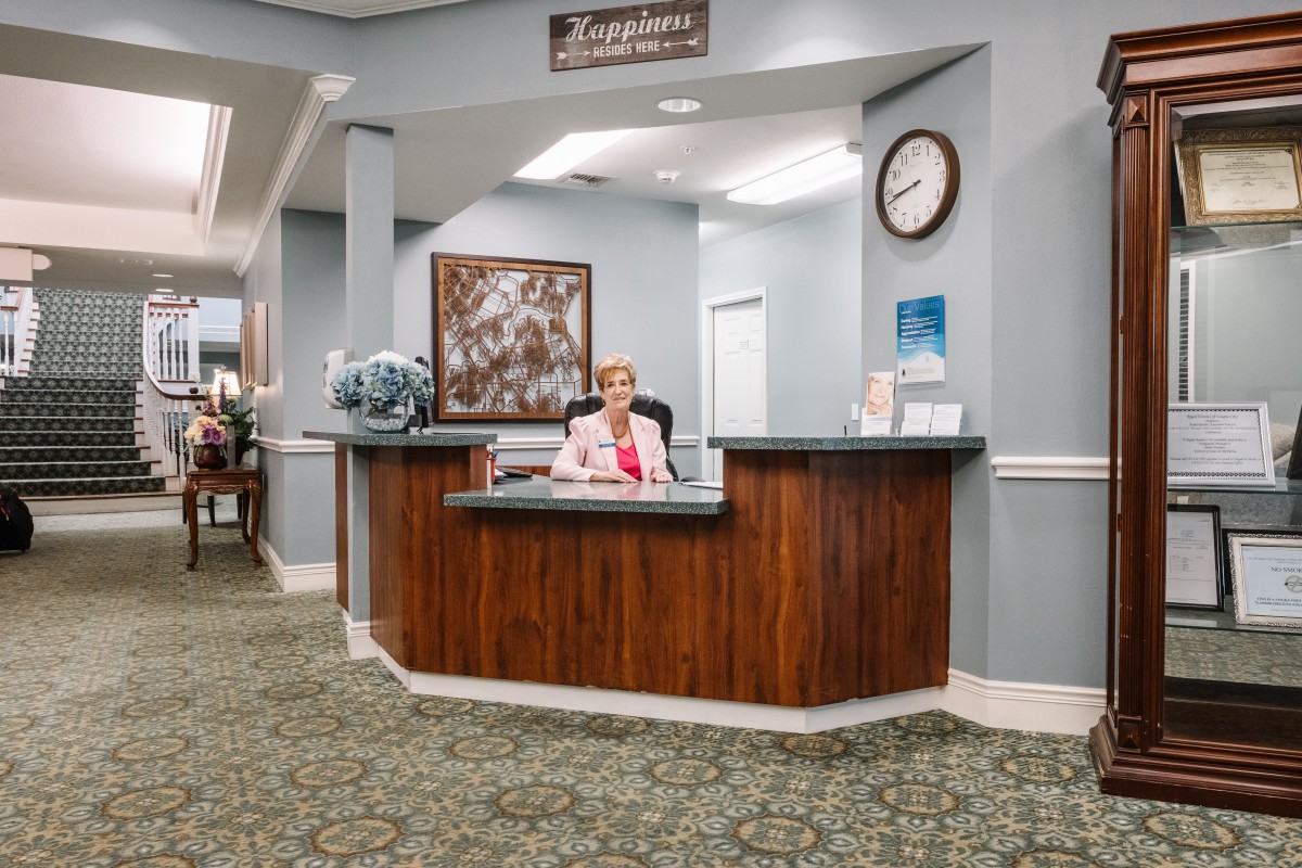 A receptionist sits at a wooden desk in a welcoming office area.