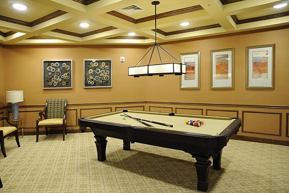 A well-lit billiard room featuring a pool table, comfortable seating, and decorative artwork on the walls.