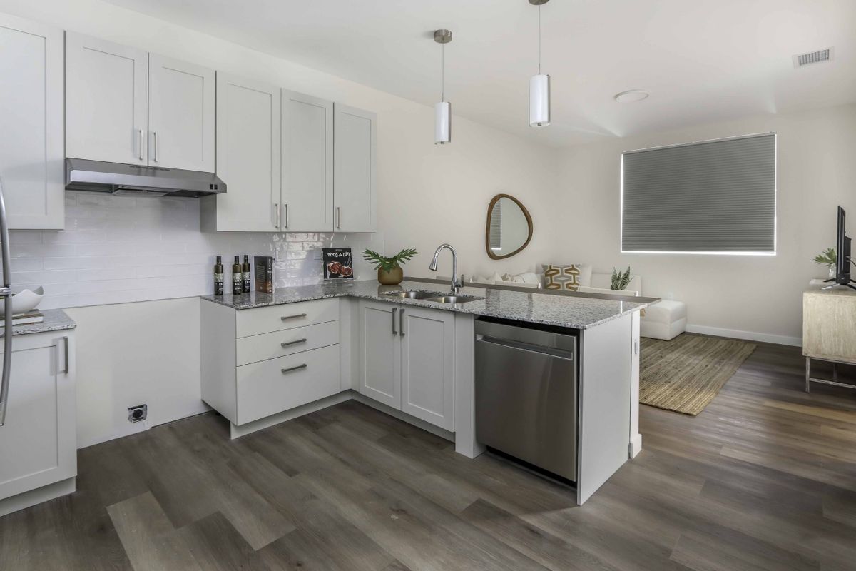 A modern kitchen with white cabinets, stainless steel appliances, and wood flooring.