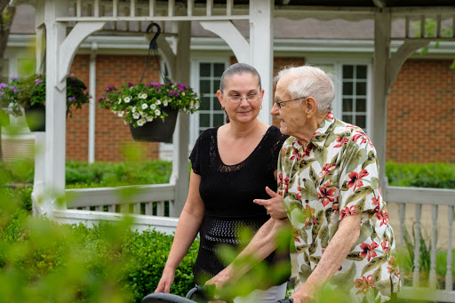 A caregiver and an elderly person enjoy a conversation in a beautifully landscaped garden.
