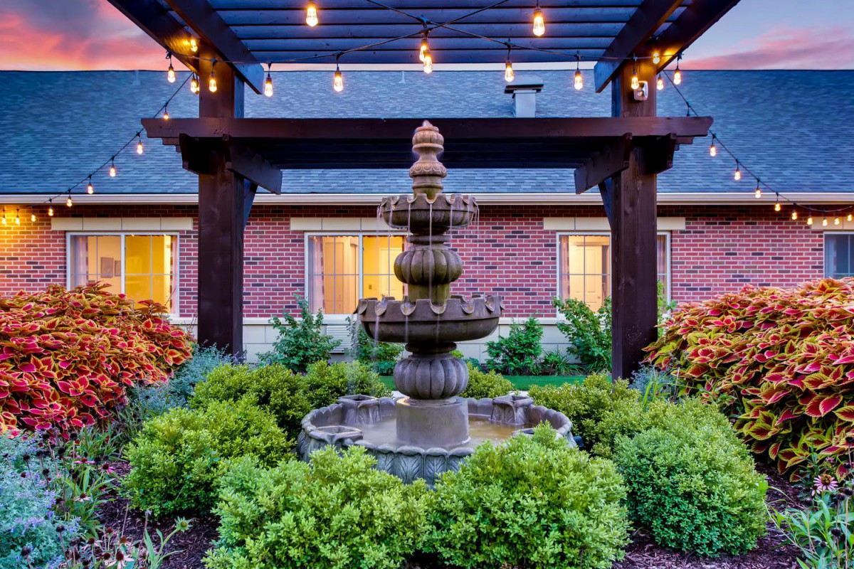 A beautifully landscaped garden with a tiered fountain and decorative lighting under a pergola.