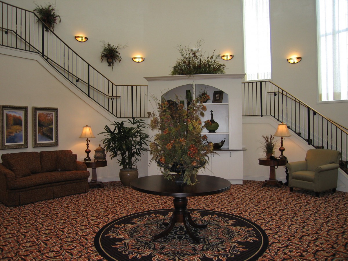 A spacious and elegantly decorated lobby with a round table centerpiece, surrounded by comfortable seating and greenery.