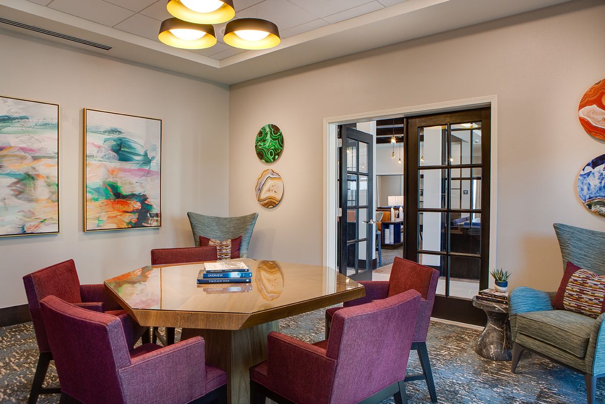 A modern dining room featuring a wooden hexagonal table surrounded by upholstered armchairs, with contemporary artwork and decorative plates on the walls.