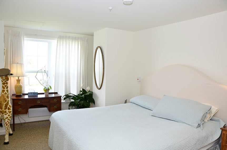 A bright and minimalist bedroom with a large bed, mirror, and window.