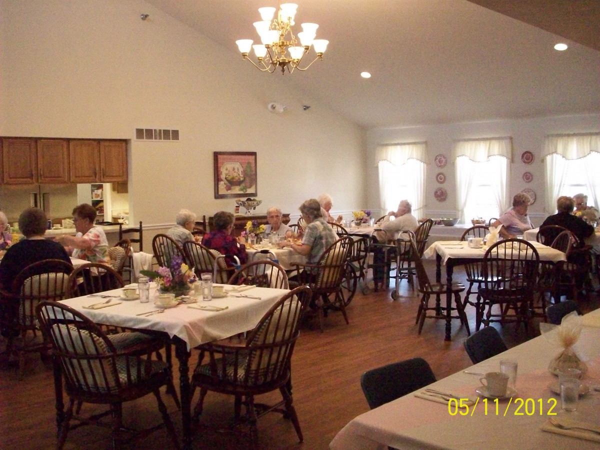 A cozy dining room with people sitting at tables, enjoying a meal under a chandelier.