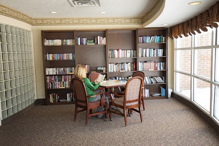 A woman reading at a table in a library with bookshelves in the background.