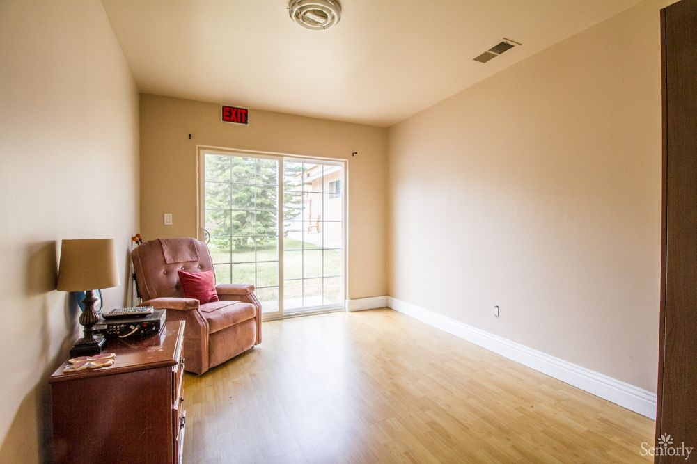 A bright and minimalist living room with wood flooring, featuring a single chair and a sliding glass door leading to the outside.