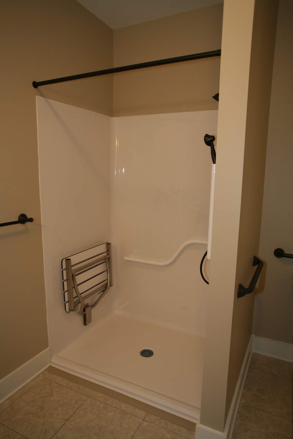 A bathroom featuring an accessible walk-in shower with grab bars and a towel rack.
