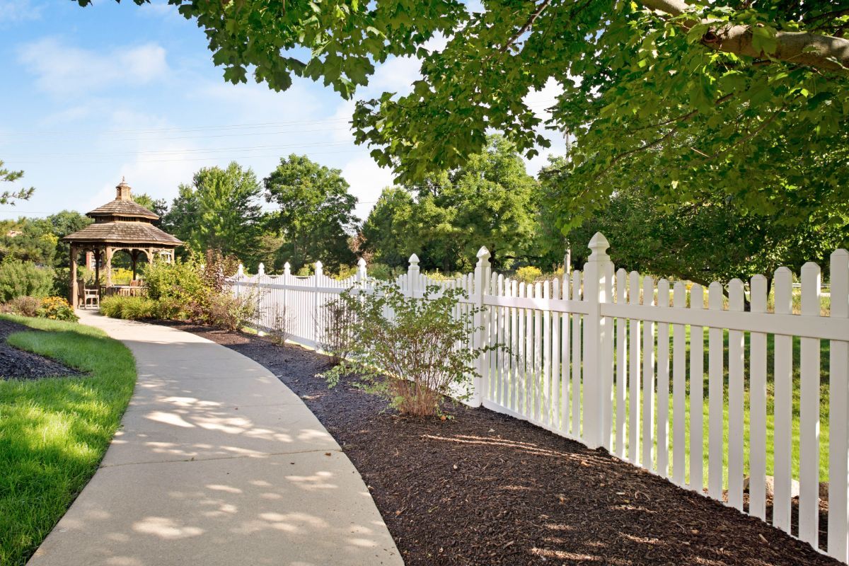 A serene garden pathway bordered by a white picket fence and lush greenery.