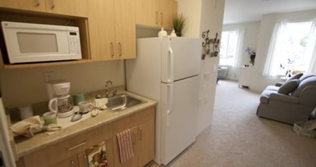 A compact kitchen space in an apartment with a refrigerator, sink, and wooden cabinets.
