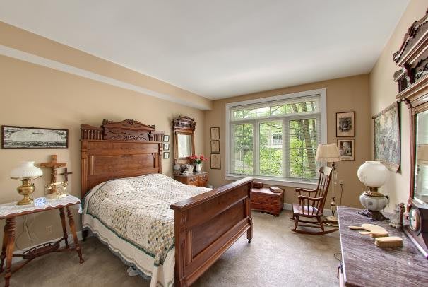 A cozy bedroom with antique wooden furniture and a large window overlooking greenery.