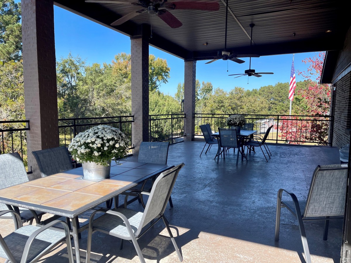 A spacious outdoor patio with tables, chairs, and ceiling fans, offering a scenic view.